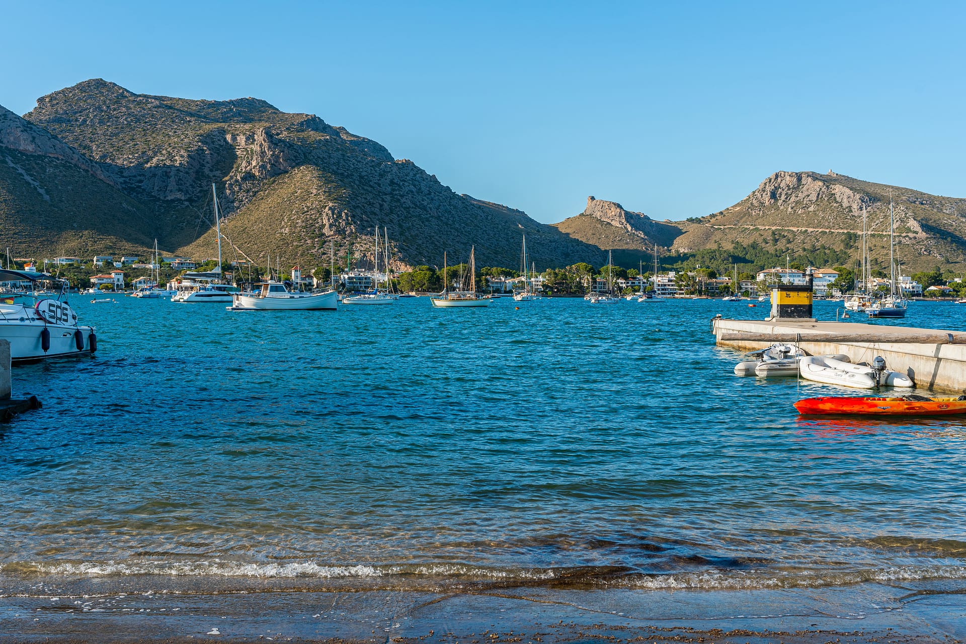 A view of sailboats and yachts in the bay of Puerto Pollensa, backed by the Serra de Tramuntana mountains.
